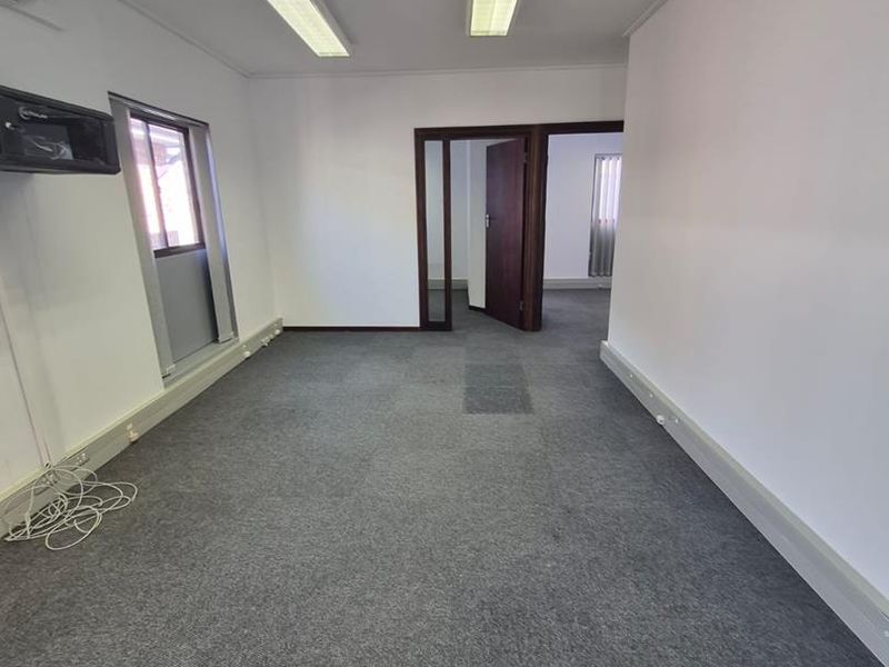 An empty office space featuring grey carpet flooring, fluorescent lighting, and an integrated air conditioning unit.
