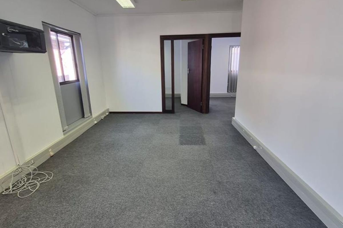 An empty office space featuring grey carpet flooring, fluorescent lighting, and an integrated air conditioning unit.