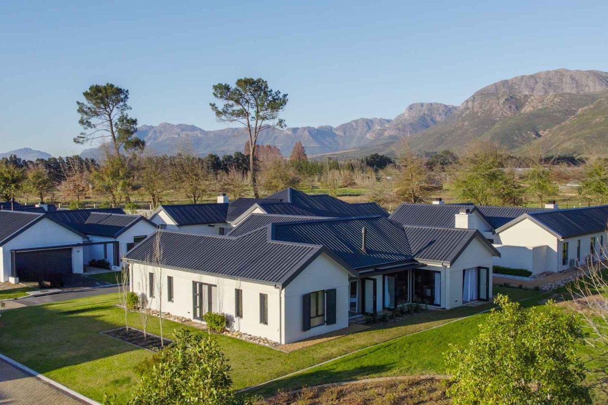 Aerial view of a modern residential property featuring a dark metal roof, well-maintained lawn, and scenic mountain backdrop.
