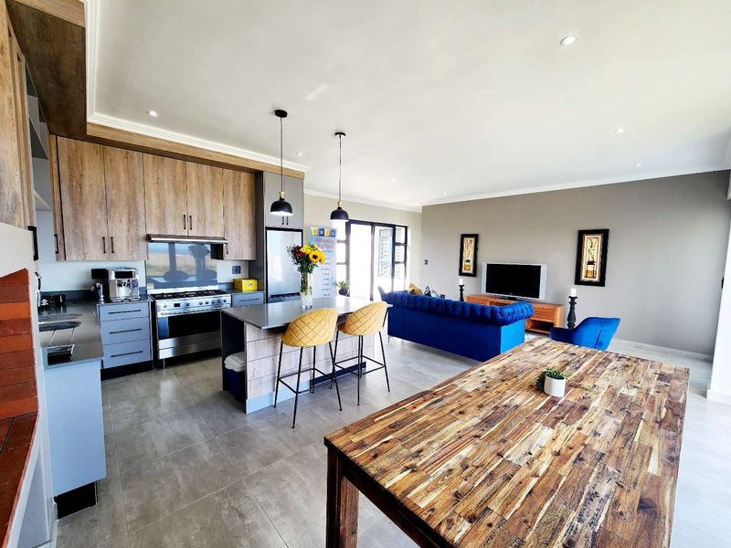 Spacious open-plan living area featuring a modern kitchen with wood-finish cabinetry, a central island, and seamless flow to the outdoor patio area.