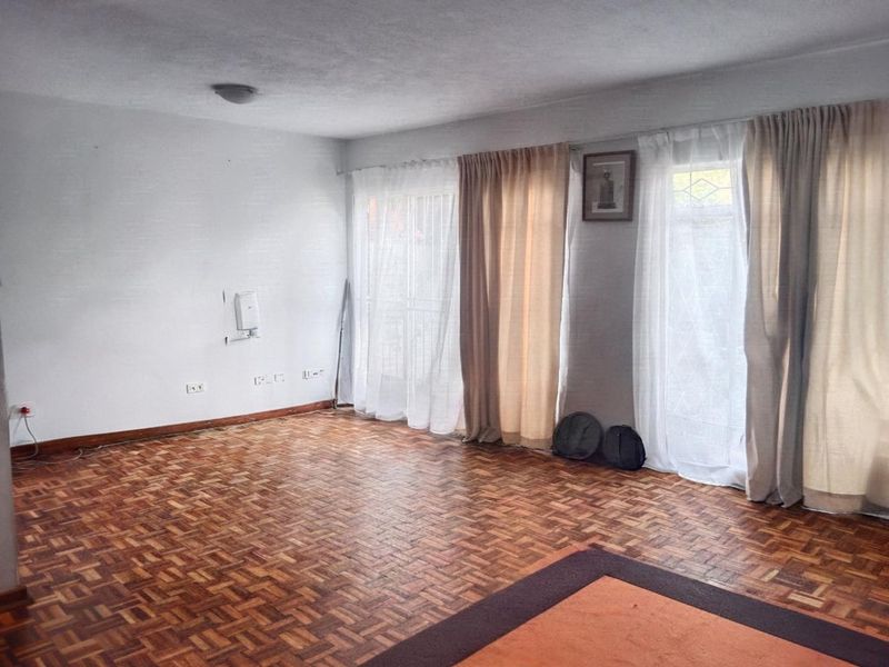 A spacious, empty living room featuring classic parquet flooring and large sliding glass doors that provide ample natural light.