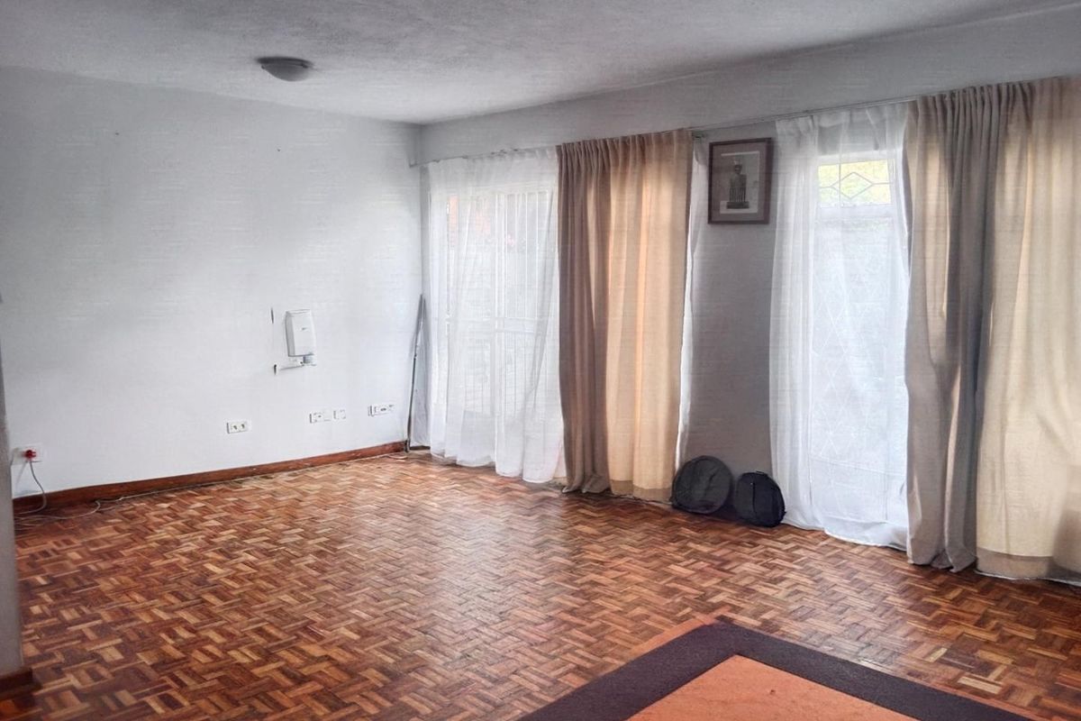 A spacious, empty living room featuring classic parquet flooring and large sliding glass doors that provide ample natural light.