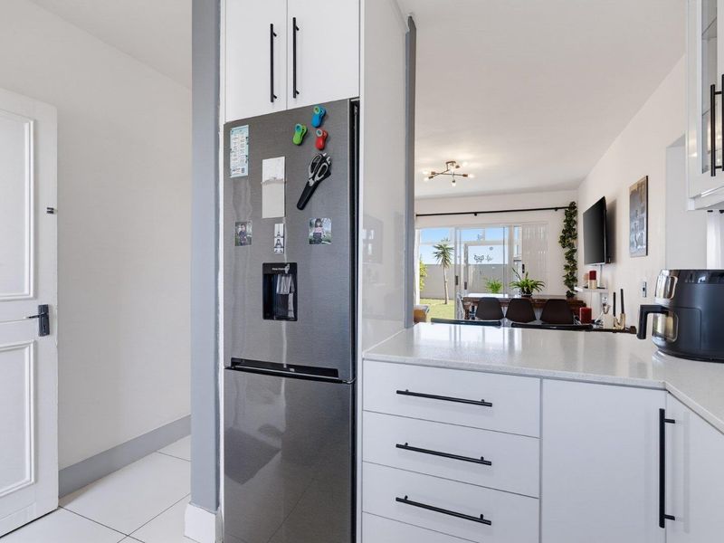 Modern open-plan kitchen featuring sleek white cabinetry, stone countertops, and tiled flooring, flowing seamlessly into the adjacent living and dining area.