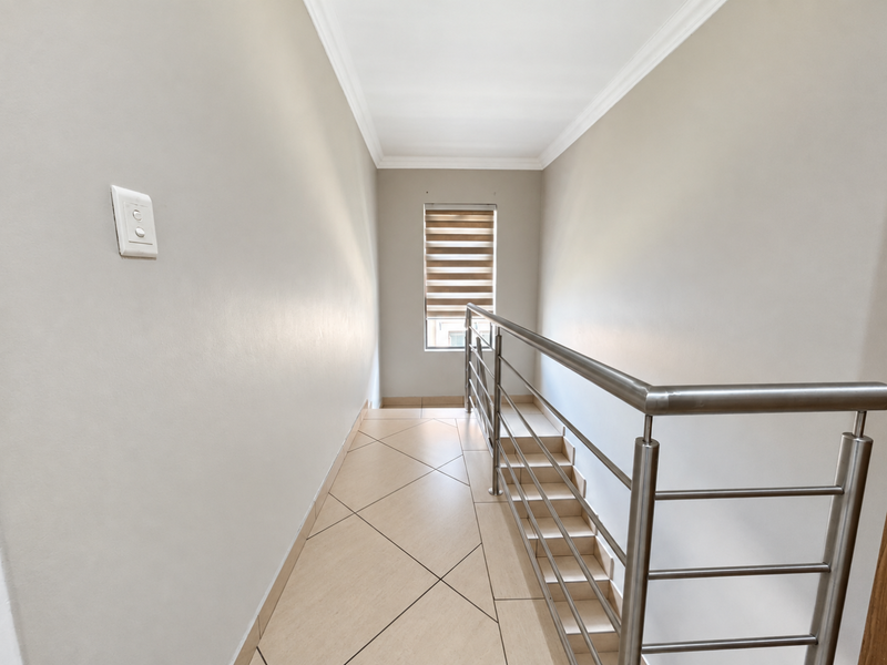 A bright, modern hallway featuring tiled flooring, a stainless steel balustrade, and a window with a roller blind.