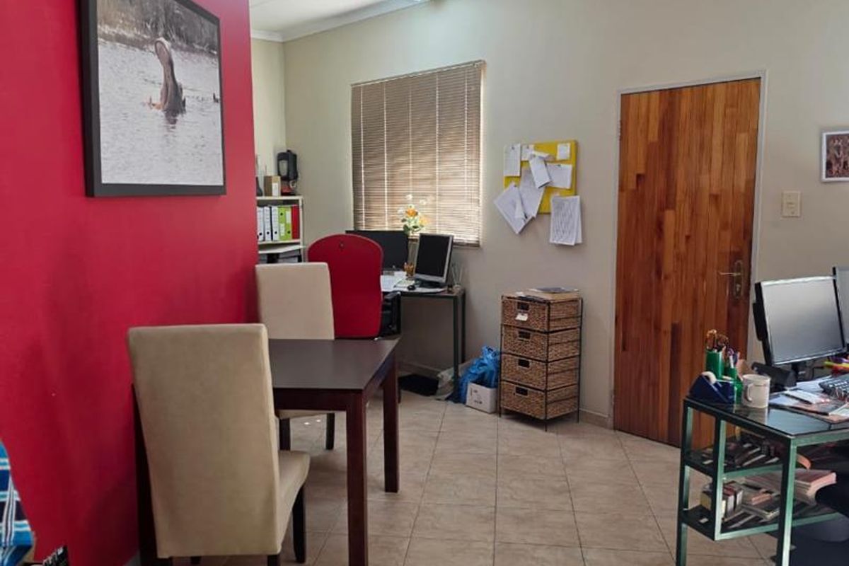A functional office space featuring tiled flooring, a prominent red accent wall, and a solid wood door.