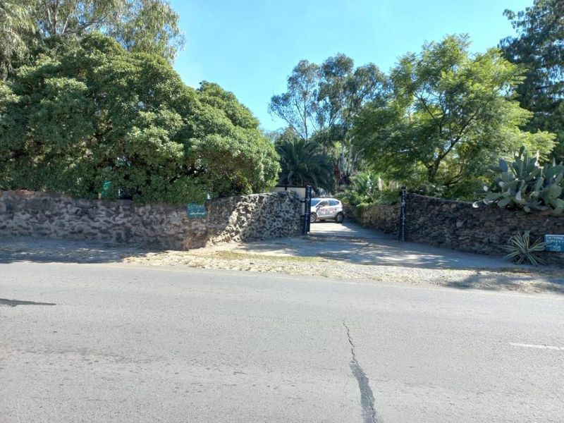 Street view of the property entrance featuring a rustic stone boundary wall and a gated driveway access point.