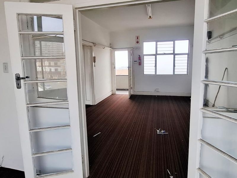 An empty office space featuring classic french doors, carpeted flooring, and large windows providing natural light.