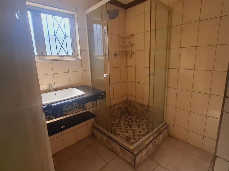 A functional bathroom featuring a glass shower enclosure, a vanity basin, and tiled finishes throughout, offering potential for a modern renovation.