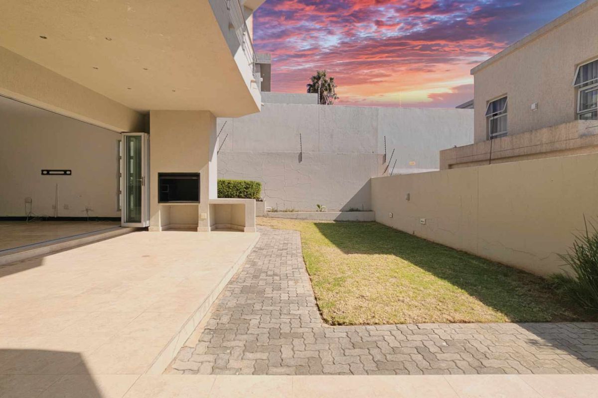 A private rear garden featuring a paved patio area with a built-in braai, seamlessly connected to the interior living space through large sliding doors.