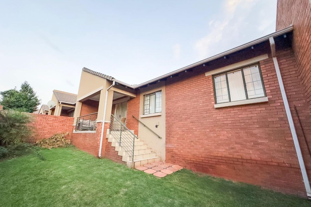 Rear view of the townhouse featuring exposed red brick facade, a raised patio area with metal railings, and a private grassed garden space.
