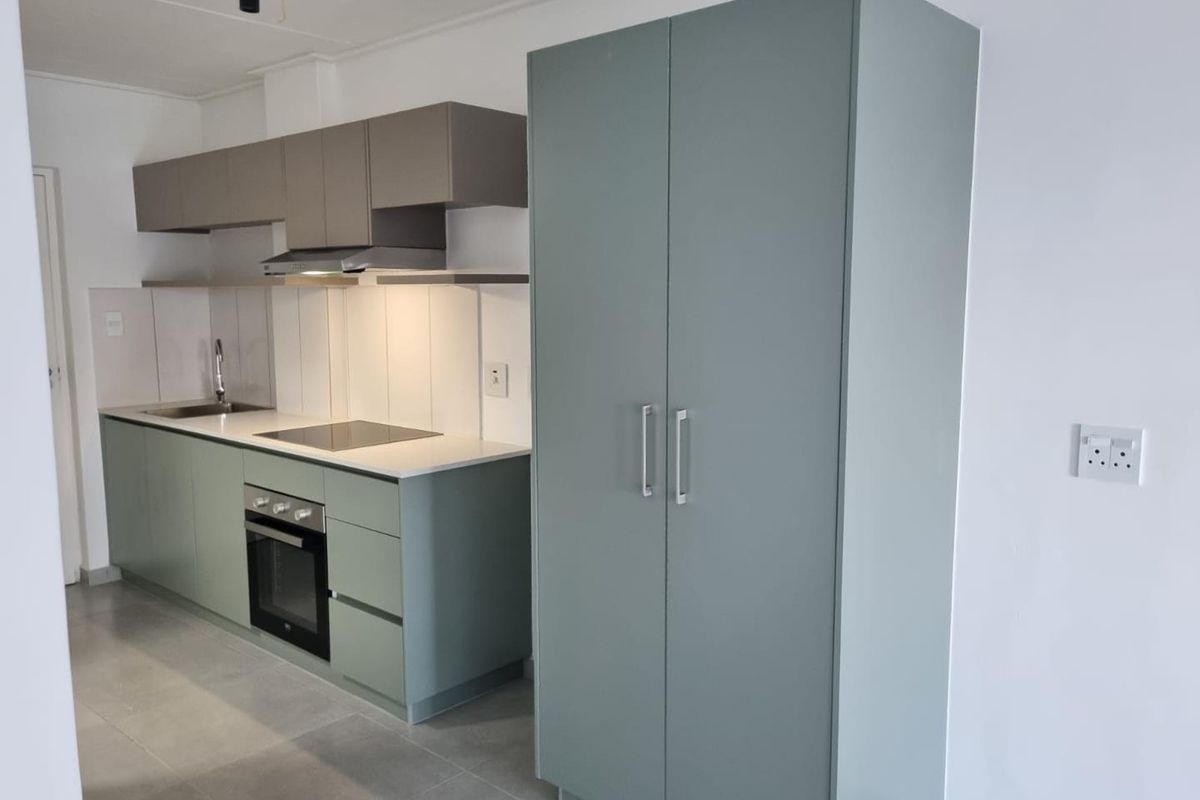 Modern kitchen featuring sage green cabinetry, integrated oven and hob, stainless steel sink, and neutral tiled flooring in a clean, minimalist space.