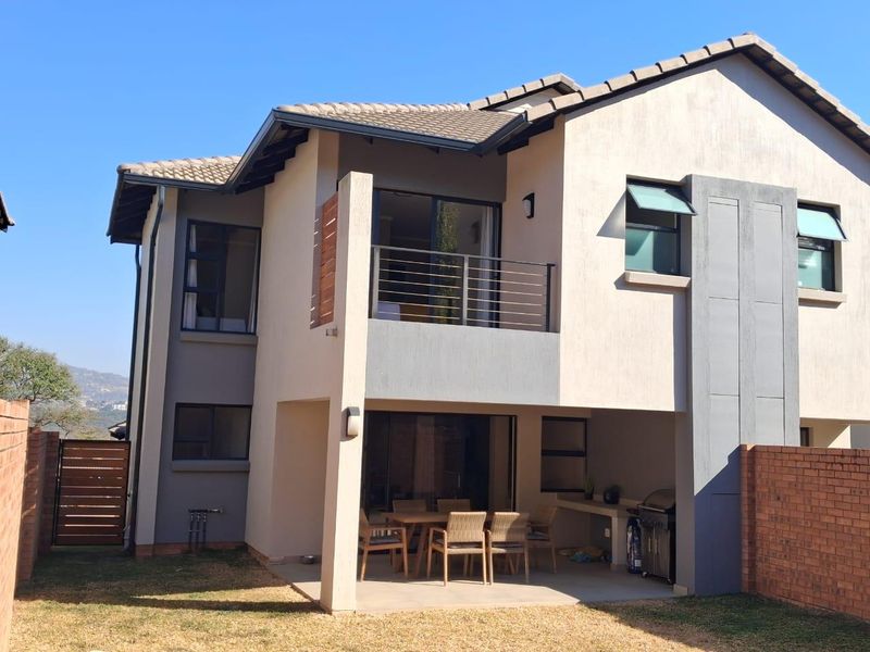 Rear view of a double-storey cluster home featuring a covered patio with built-in braai, an upper-level balcony, and a private garden area.
