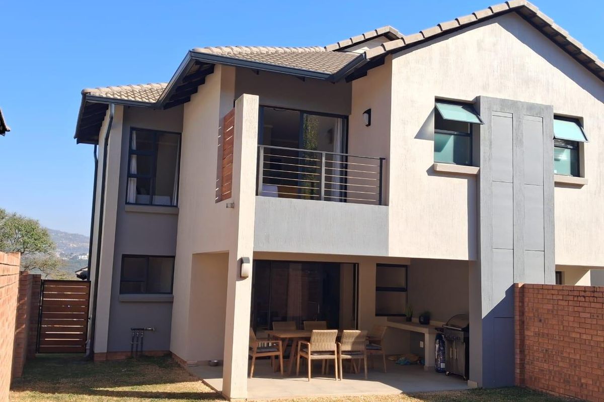 Rear view of a double-storey cluster home featuring a covered patio with built-in braai, an upper-level balcony, and a private garden area.