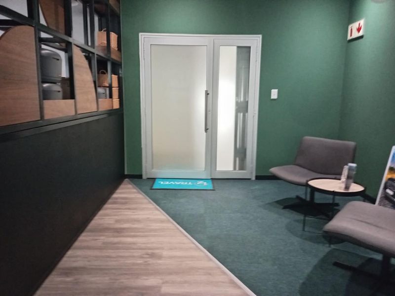A modern office reception area featuring a frosted glass entrance door, dual-tone flooring, and built-in shelving units against a green accent wall.