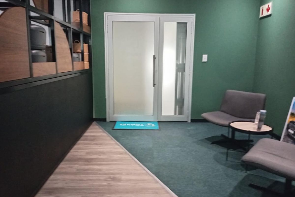 A modern office reception area featuring a frosted glass entrance door, dual-tone flooring, and built-in shelving units against a green accent wall.