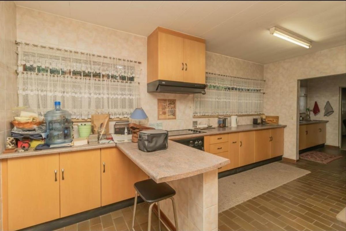 A dated kitchen featuring wood-finish cabinetry, a breakfast bar, integrated hob and extractor fan, and tiled flooring with an adjacent scullery area.