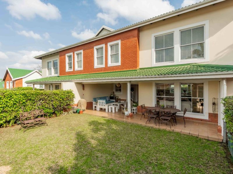 Rear view of the townhouse featuring a covered patio, tiled flooring, and a private garden area with established hedges.