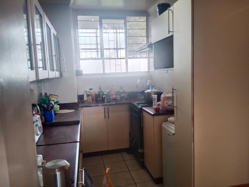 A functional galley-style kitchen featuring laminate countertops, built-in cabinetry, a freestanding stove with extractor fan, and tiled flooring.