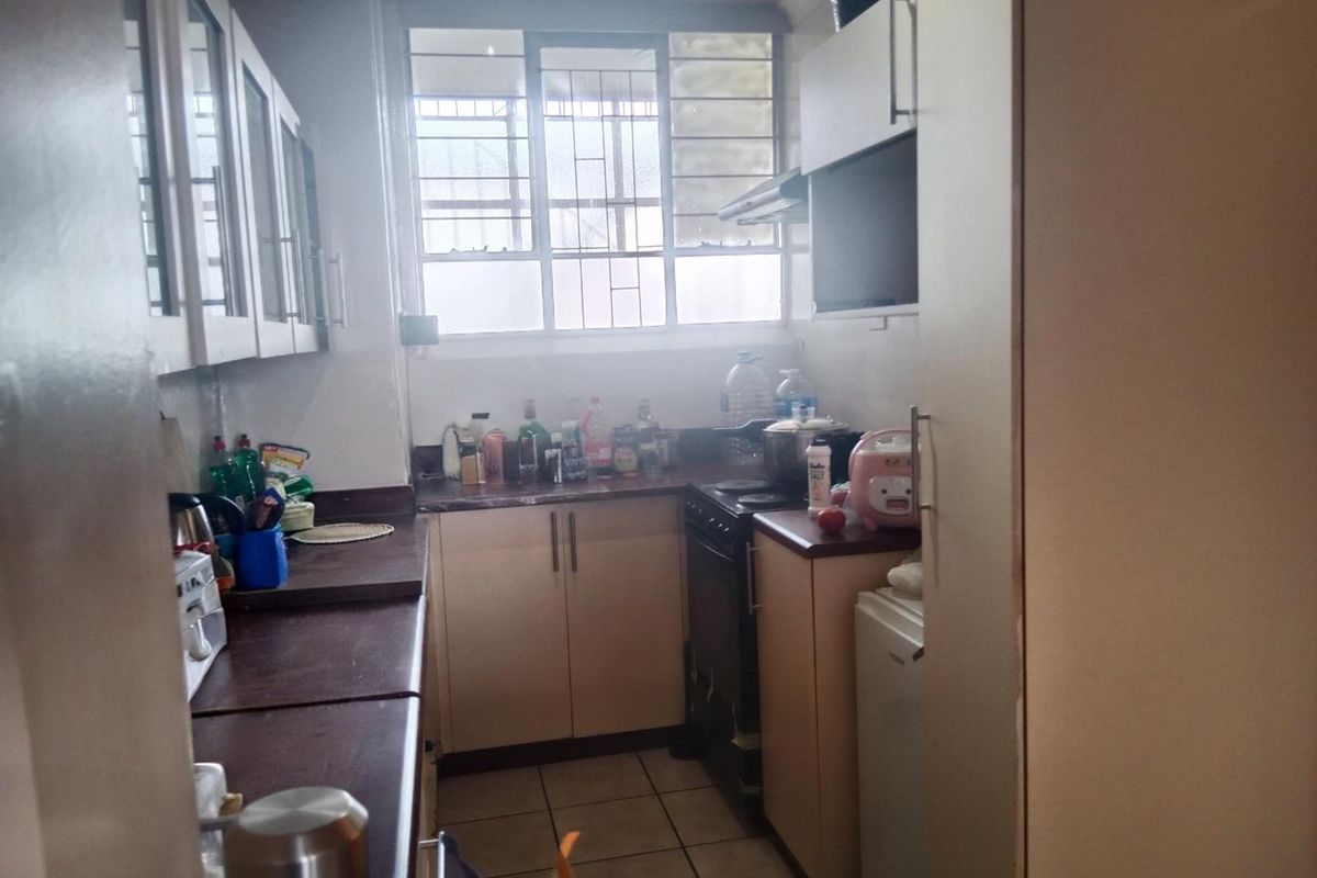 A functional galley-style kitchen featuring laminate countertops, built-in cabinetry, a freestanding stove with extractor fan, and tiled flooring.
