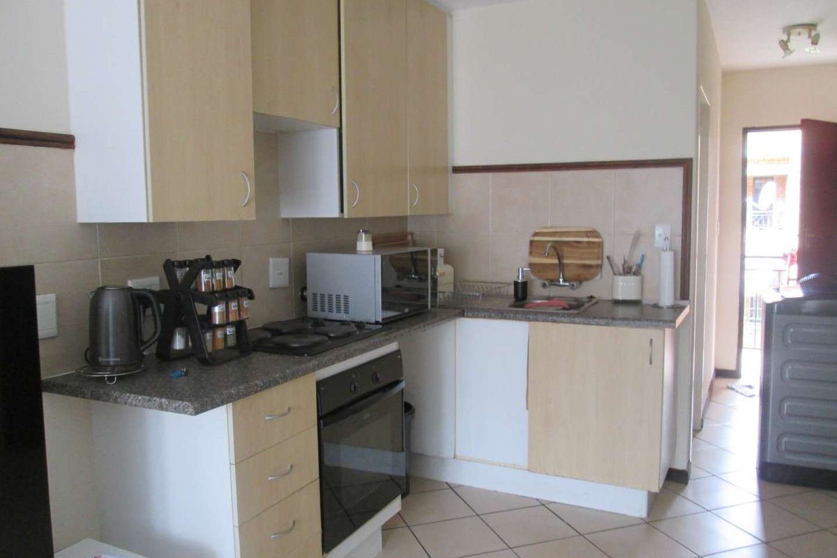 A functional kitchen featuring light wood-tone cabinetry, granite-look countertops, a built-in oven, and a hob, with tiled flooring throughout.