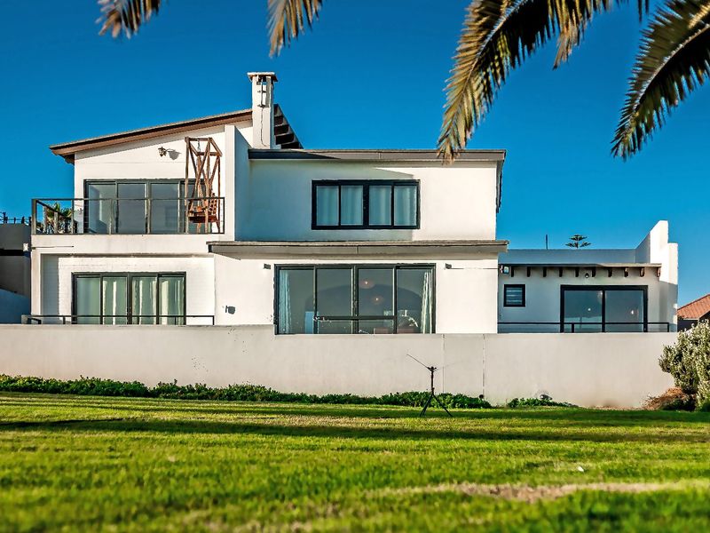 Rear view of a multi-level residential property featuring a white facade, balcony, and sliding glass doors overlooking a private lawn.