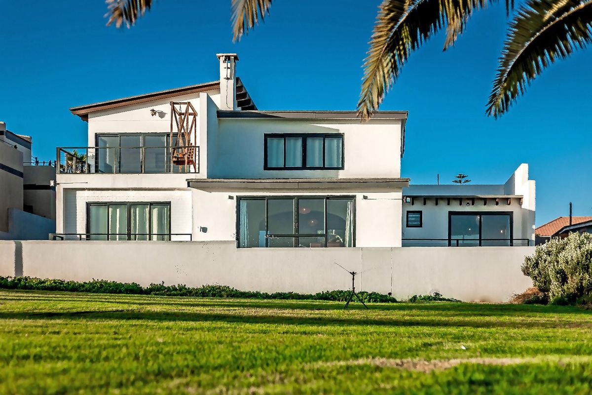 Rear view of a multi-level residential property featuring a white facade, balcony, and sliding glass doors overlooking a private lawn.