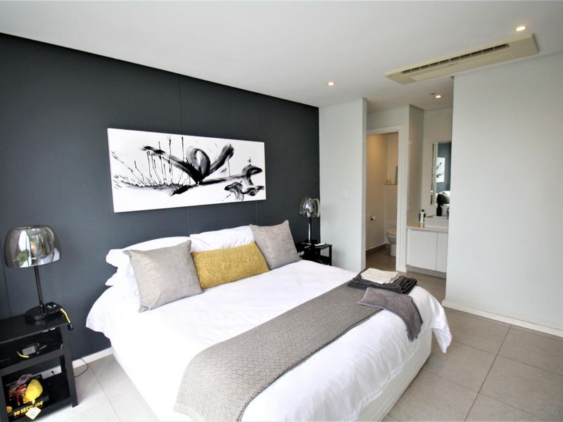 Modern bedroom featuring tiled flooring, recessed downlighting, ducted air conditioning, and an adjoining en-suite bathroom with a vanity.