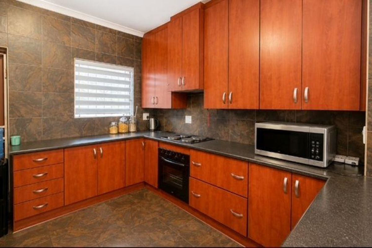 A functional kitchen featuring warm-toned wooden cabinetry, dark laminate countertops, a built-in oven, and a tiled splashback with matching floor tiles.