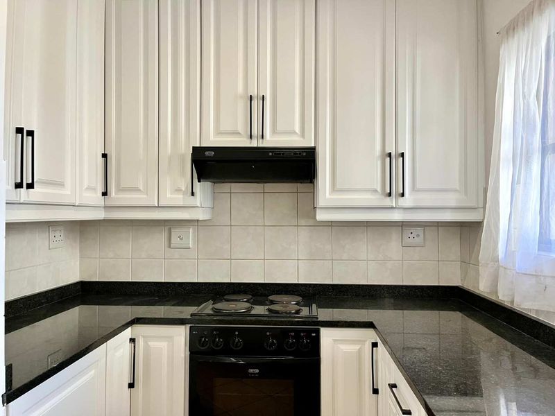 A well-maintained kitchen featuring white cabinetry, black granite countertops, a built-in oven, and an electric hob with a tiled backsplash.
