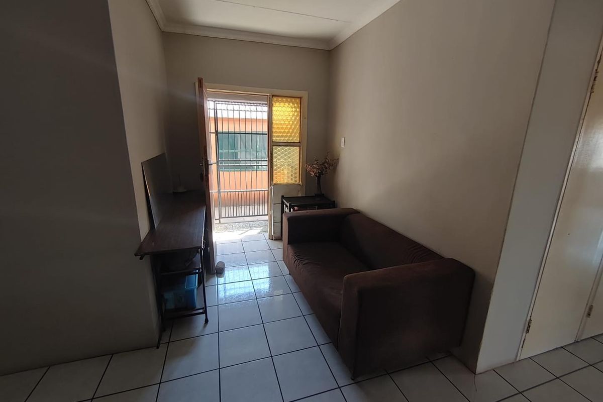 A living area featuring tiled flooring, cornicing, and direct access to an exterior space through a security gate.