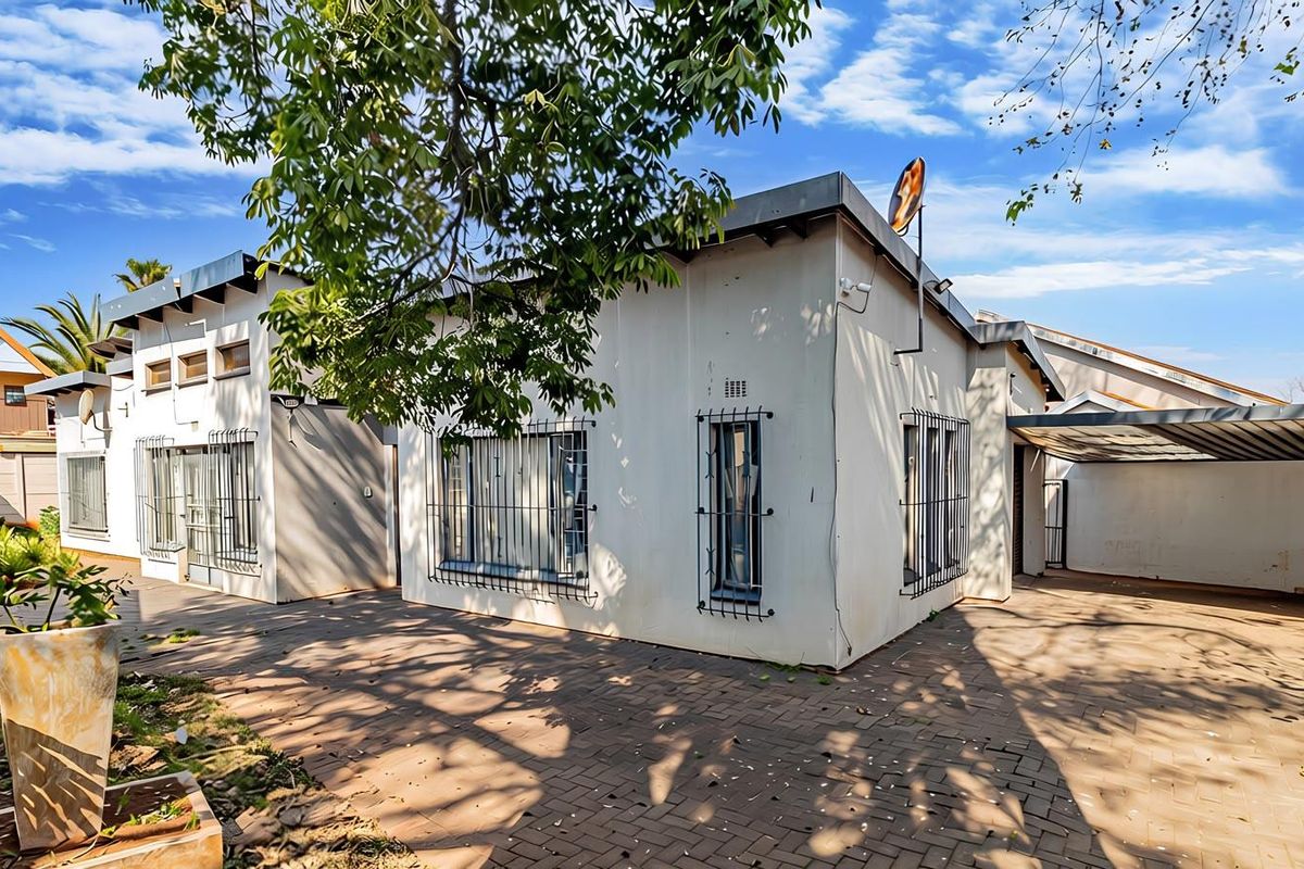 Rear exterior view of the house featuring a paved driveway, carport, and security bars on the windows.