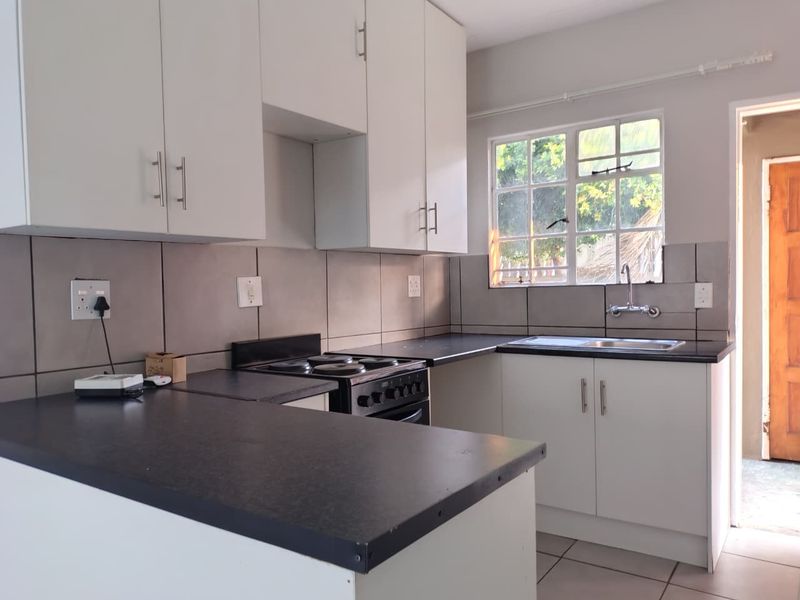 A clean, functional kitchen featuring white cabinetry, dark laminate countertops, a built-in electric stove, and a stainless steel sink with a window view.
