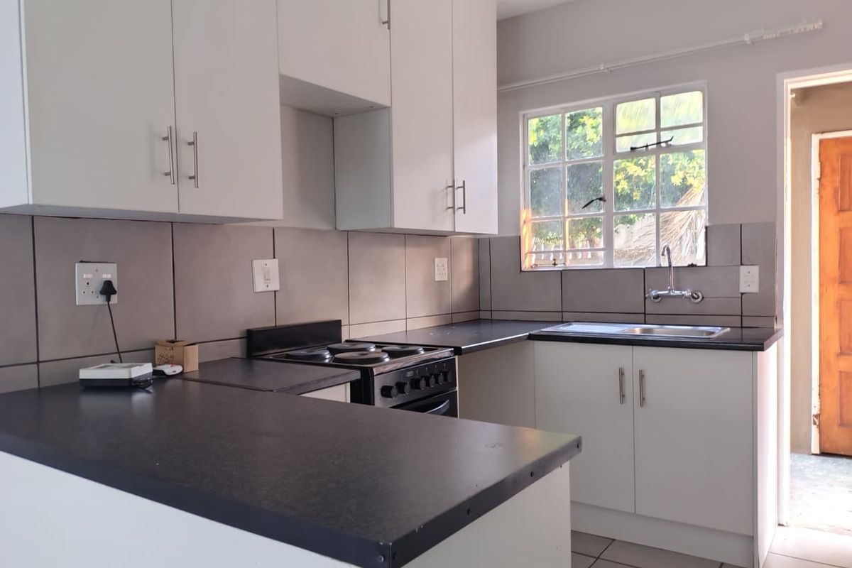 A clean, functional kitchen featuring white cabinetry, dark laminate countertops, a built-in electric stove, and a stainless steel sink with a window view.