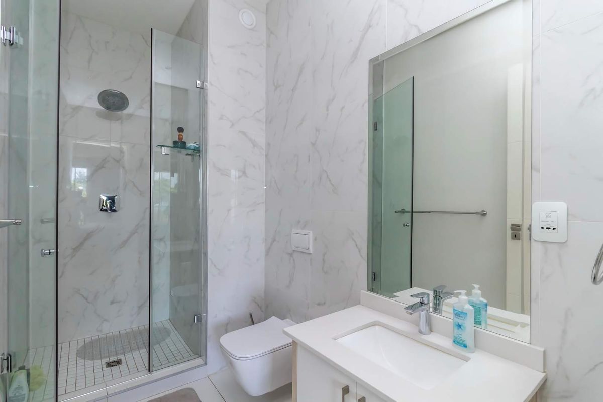 Modern bathroom featuring a glass-enclosed shower with rain head, wall-mounted toilet, and a vanity with integrated sink and large mirror.