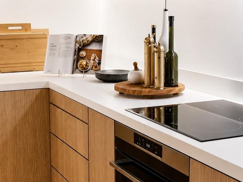 Modern kitchen featuring light oak cabinetry, sleek white countertops, and integrated induction cooktop with built-in oven.