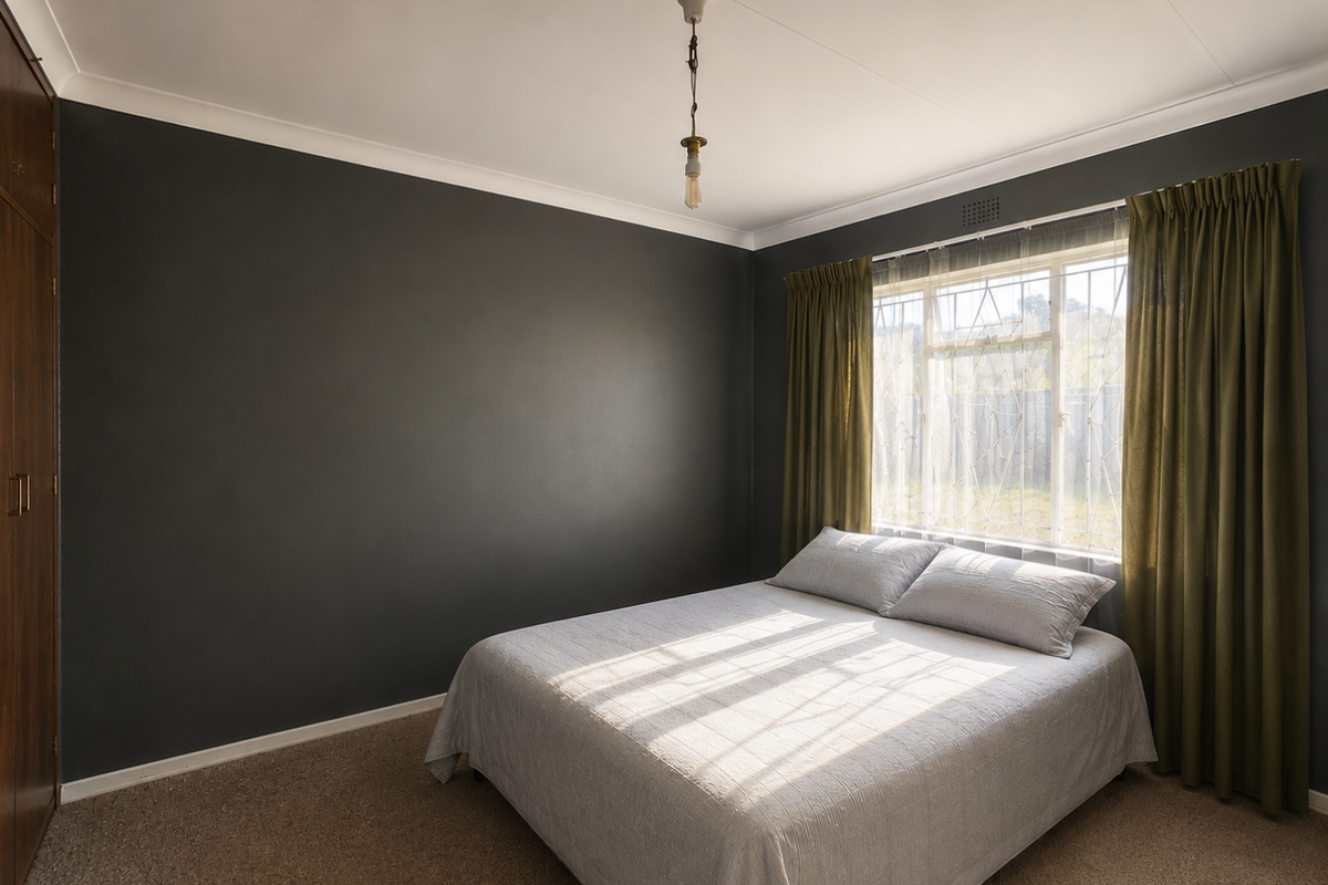 A bedroom featuring dark accent walls, built-in wooden cabinetry, and a window fitted with security bars and curtains.