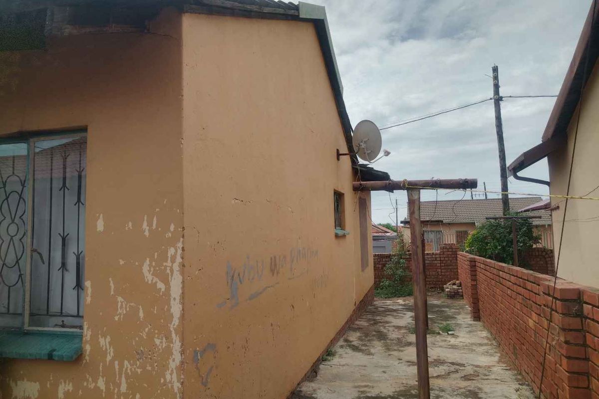 Side exterior view of the house showing a concrete pathway, brick boundary wall, and satellite dish installation.