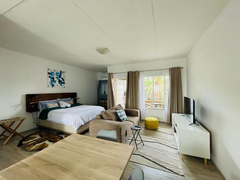 An open-plan studio apartment featuring laminate flooring, air conditioning, and a sliding glass door providing access to an outdoor patio area.