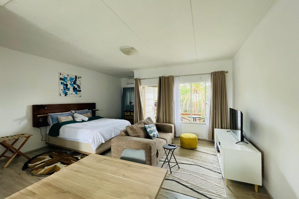 An open-plan studio apartment featuring laminate flooring, air conditioning, and a sliding glass door providing access to an outdoor patio area.
