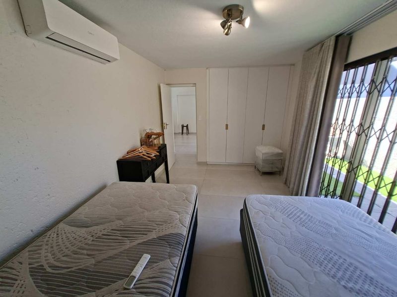 A well-lit bedroom featuring built-in cupboards, tiled flooring, and a split-system air conditioner, with direct access to an outdoor area through a sliding door.