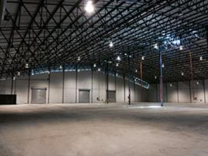 Spacious industrial warehouse featuring high ceilings with exposed steel trusses, concrete flooring, and multiple roller shutter doors for efficient access.