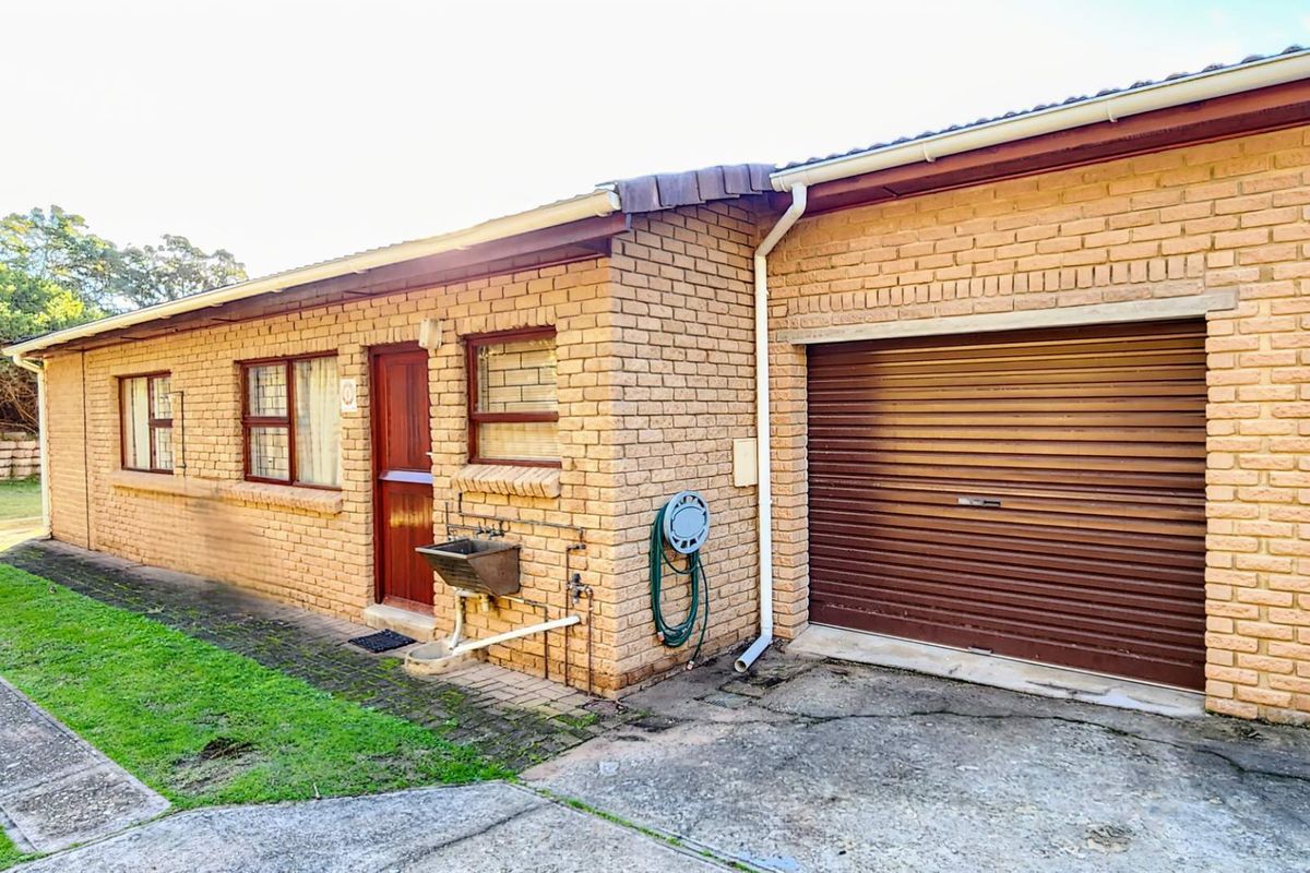 Exterior view of the property featuring face-brick facade, a single roller-door garage, and a functional outdoor utility sink.