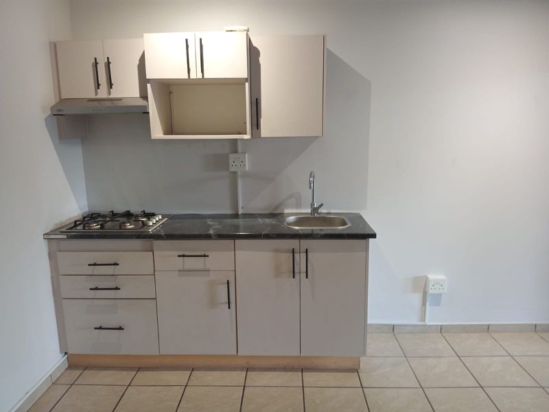 A compact, modern kitchen featuring light-toned cabinetry, a gas hob, extractor fan, and a stainless steel sink with tiled flooring.