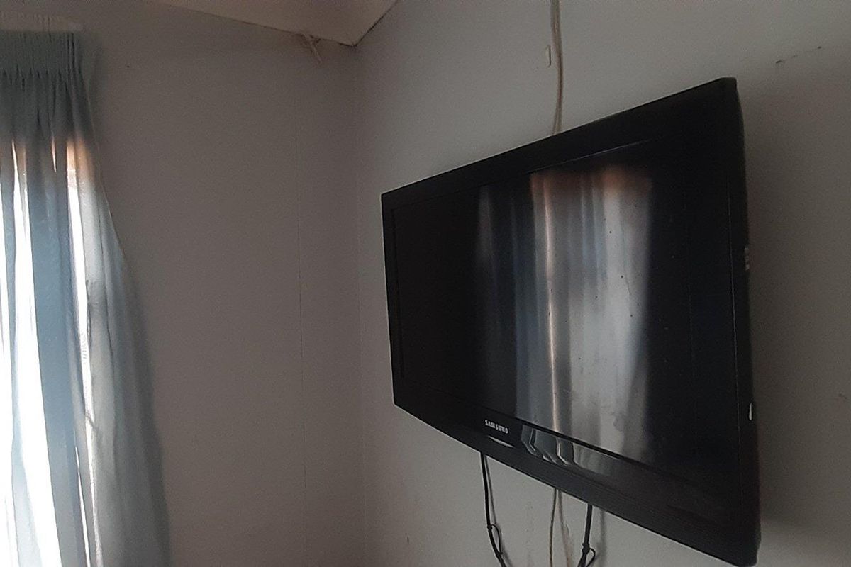 A close-up view of a wall-mounted television in a room with basic window treatments.