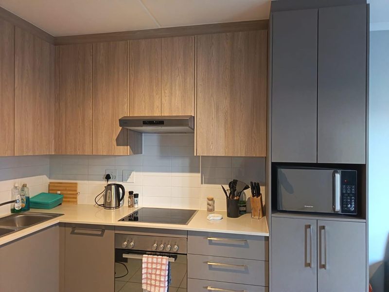 Modern kitchen featuring wood-grain and grey cabinetry, integrated appliances including an oven, hob, extractor fan, and built-in microwave with a clean tiled backsplash.