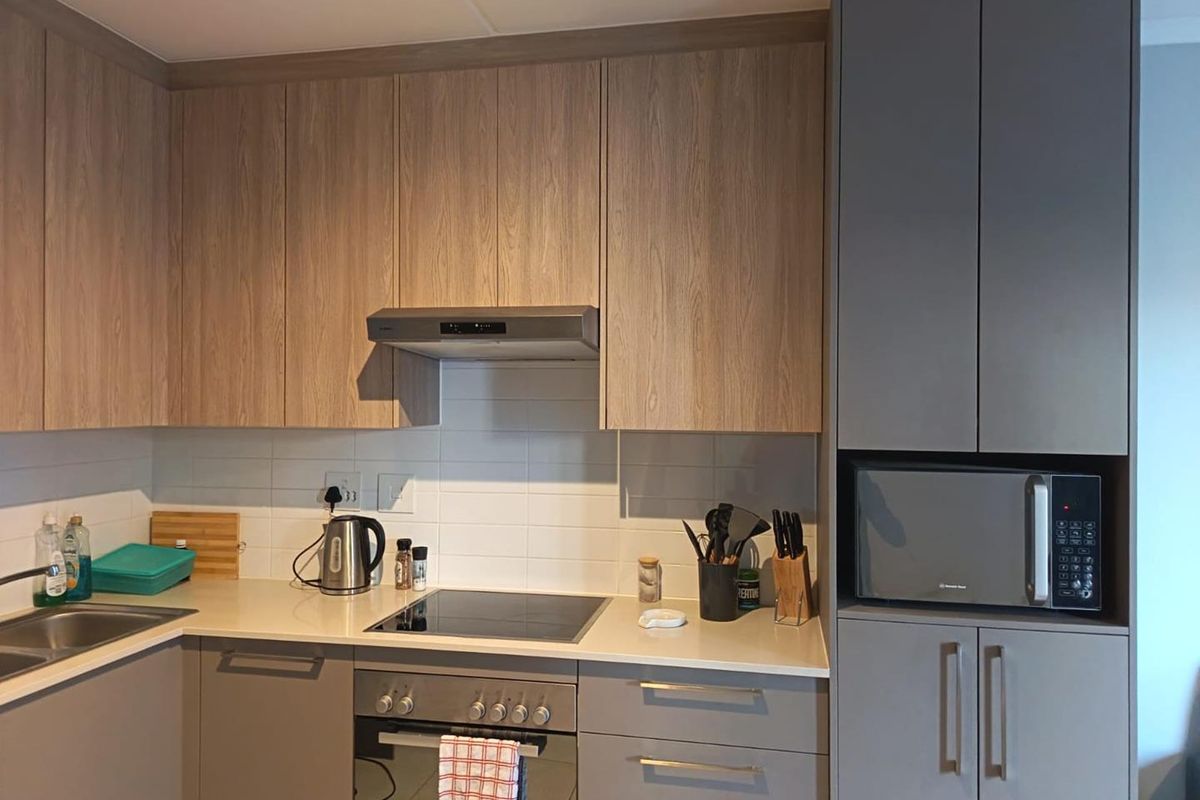 Modern kitchen featuring wood-grain and grey cabinetry, integrated appliances including an oven, hob, extractor fan, and built-in microwave with a clean tiled backsplash.