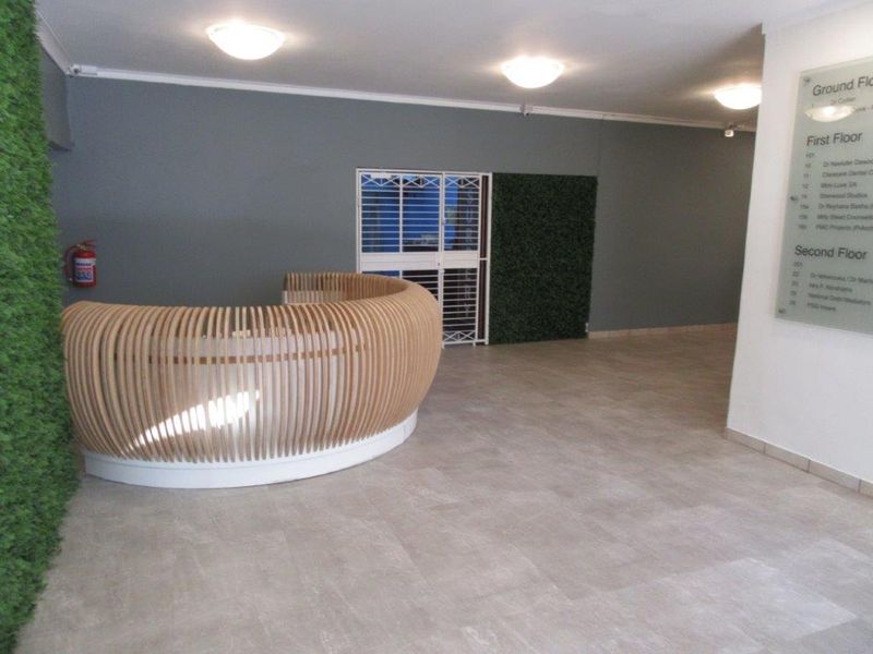 A professional building entrance featuring a modern curved reception desk, directory signage, security gate, and decorative green wall accents.
