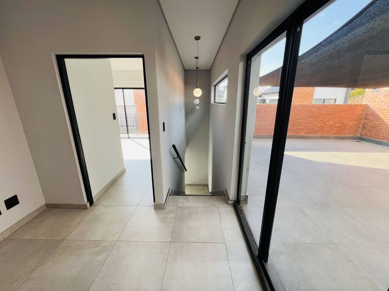 A modern, bright hallway featuring tiled flooring, a staircase with a sleek handrail, and large sliding glass doors leading to an outdoor patio area.