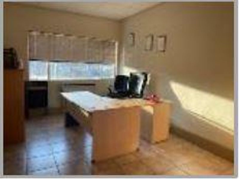 A functional office space featuring tiled flooring and a large window with blinds, providing natural light for a productive work environment.