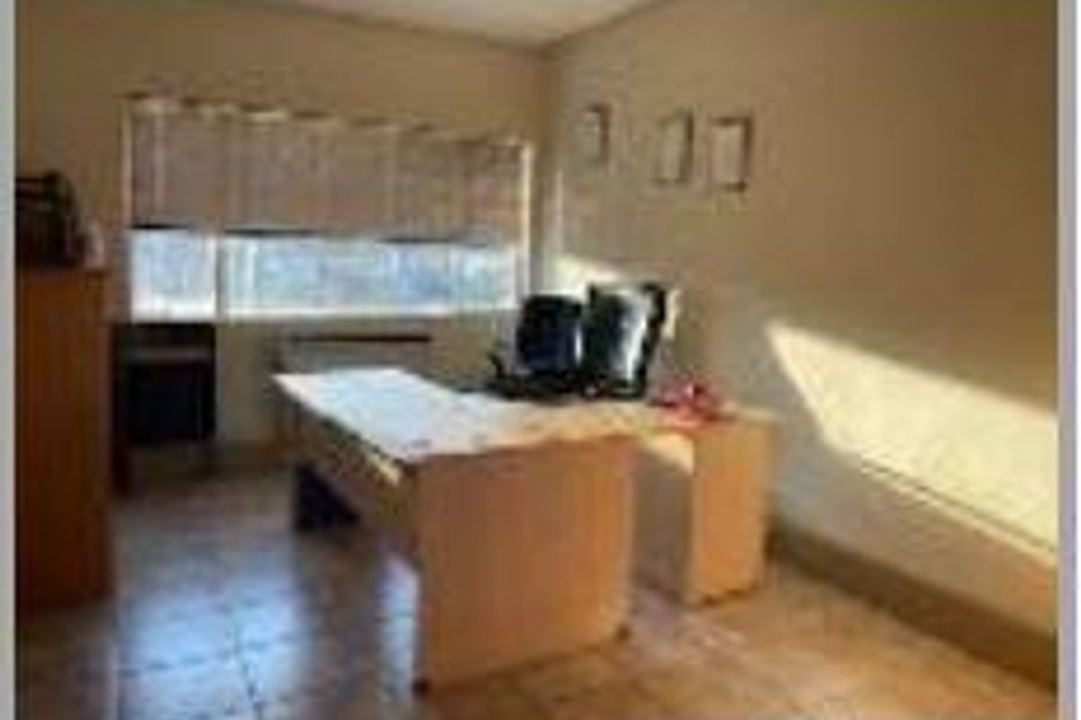 A functional office space featuring tiled flooring and a large window with blinds, providing natural light for a productive work environment.